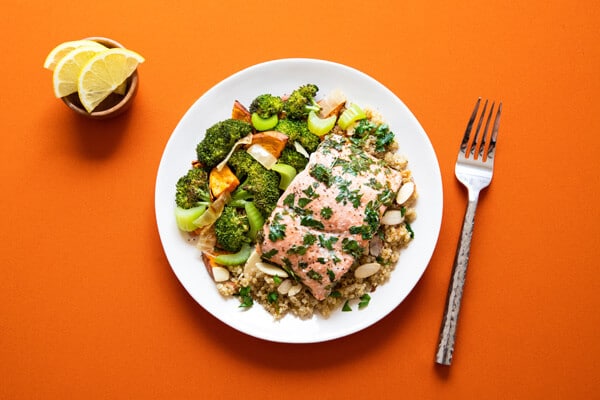 assiette brocolis, carottes, oignons, saumon, céréales, fourchette à droite de l'assiette, petit bol avec rondelles de citron
