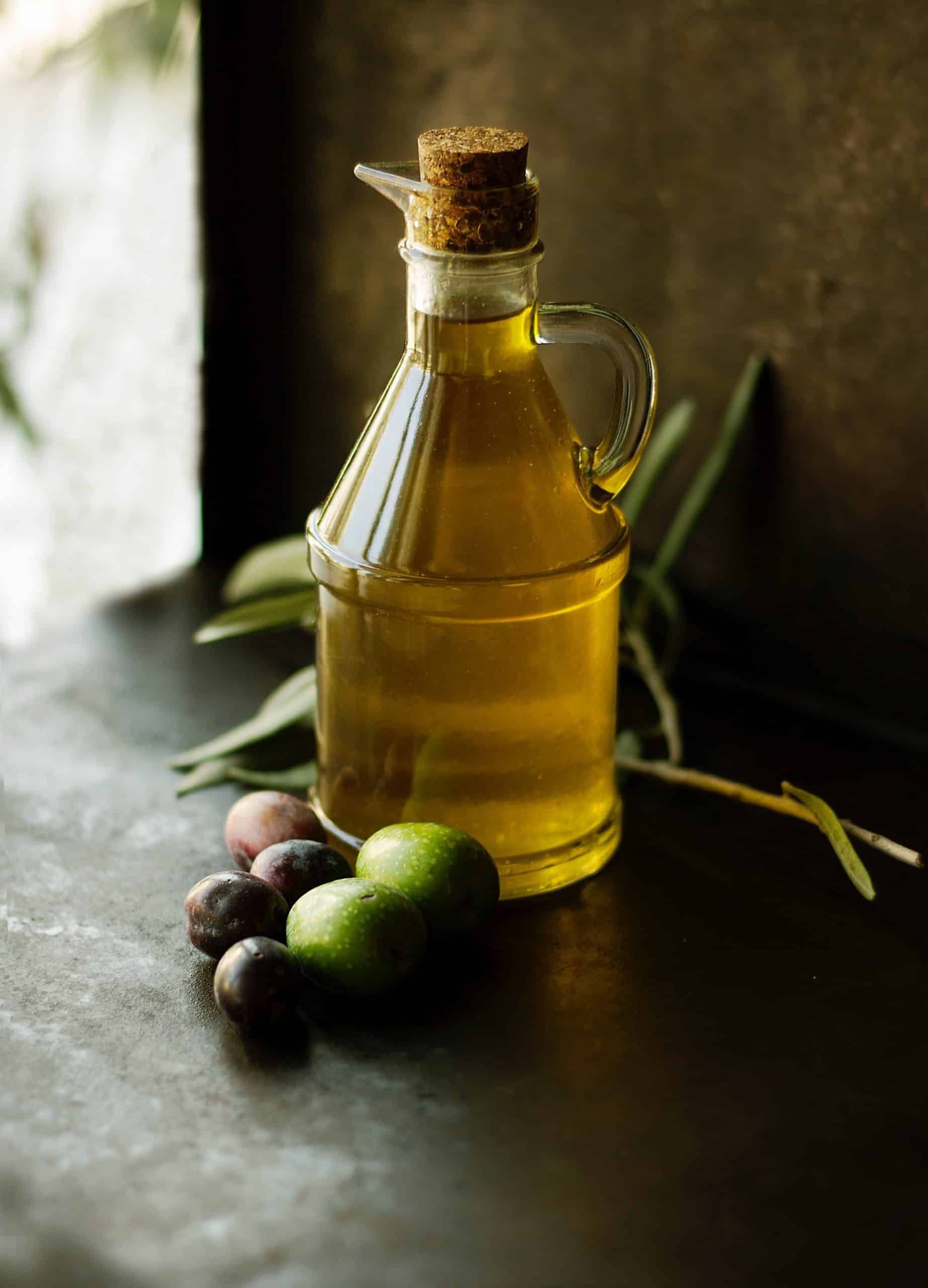 Flacon d'huile posé sur une table, olives, branche d'olivier