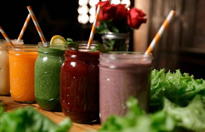 Cinq smoothies aux couleurs variées, préparés à base de fruits et de légumes frais, présentés dans des bocaux en verre avec des pailles.